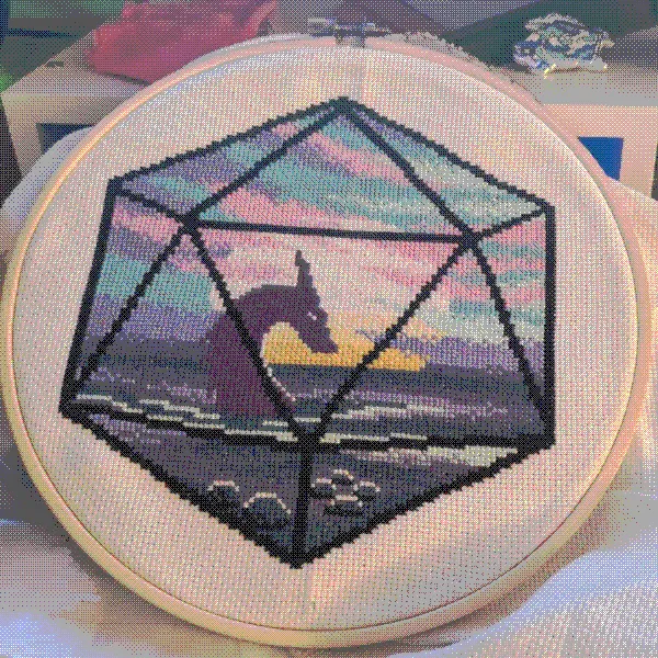 cross stitch of a dragon poking its head out of the ocean with a sunset behind it