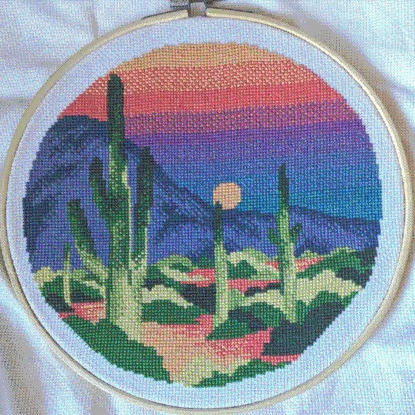 cross stitch of a desert scene with saguaro cactus and mountains with a rainbow color palette